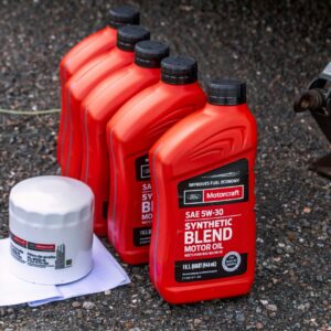 Containers of motor oil and a fuel filter sit on the pavement next to a jack.